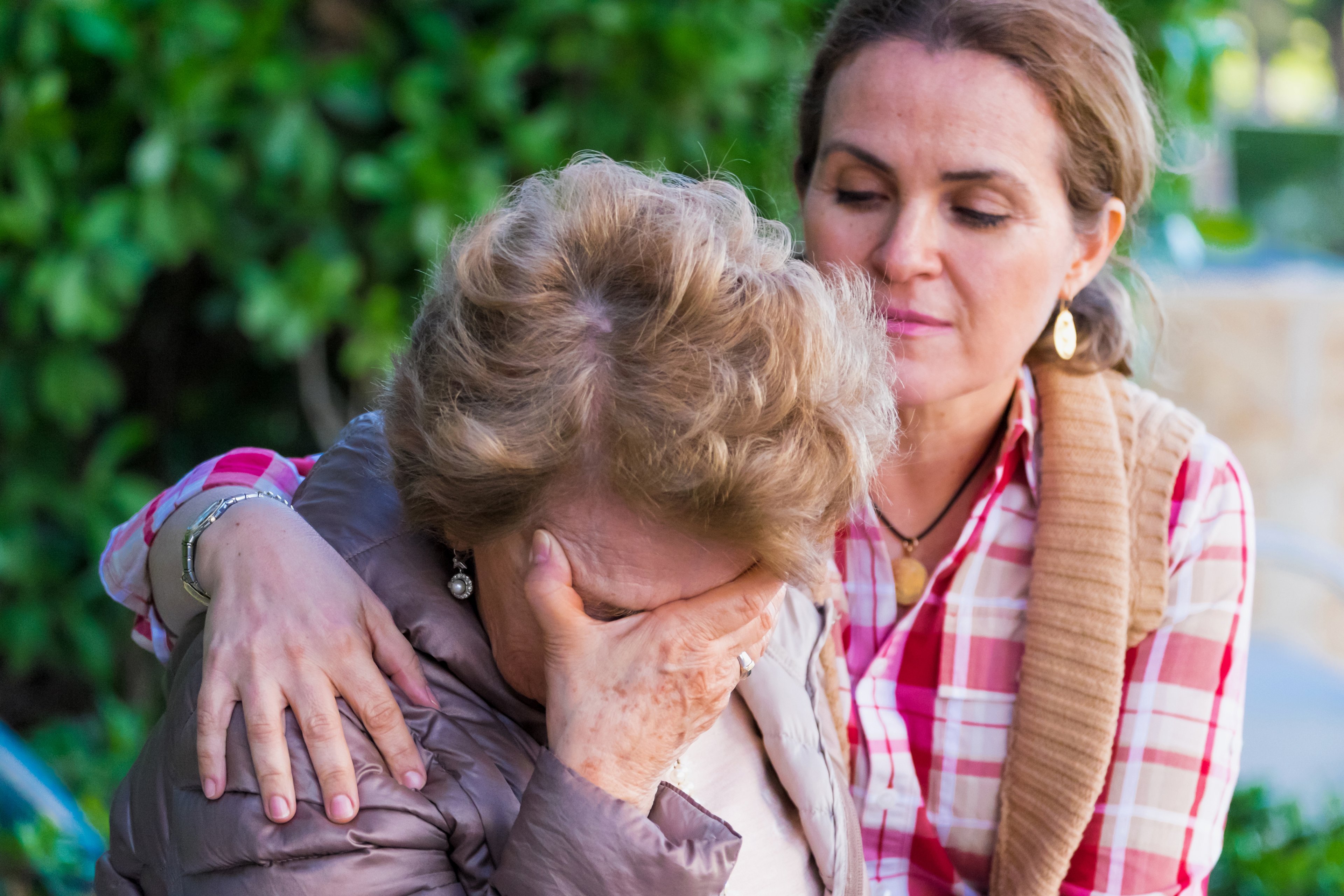 A senior is consoled by a younger person in a park.