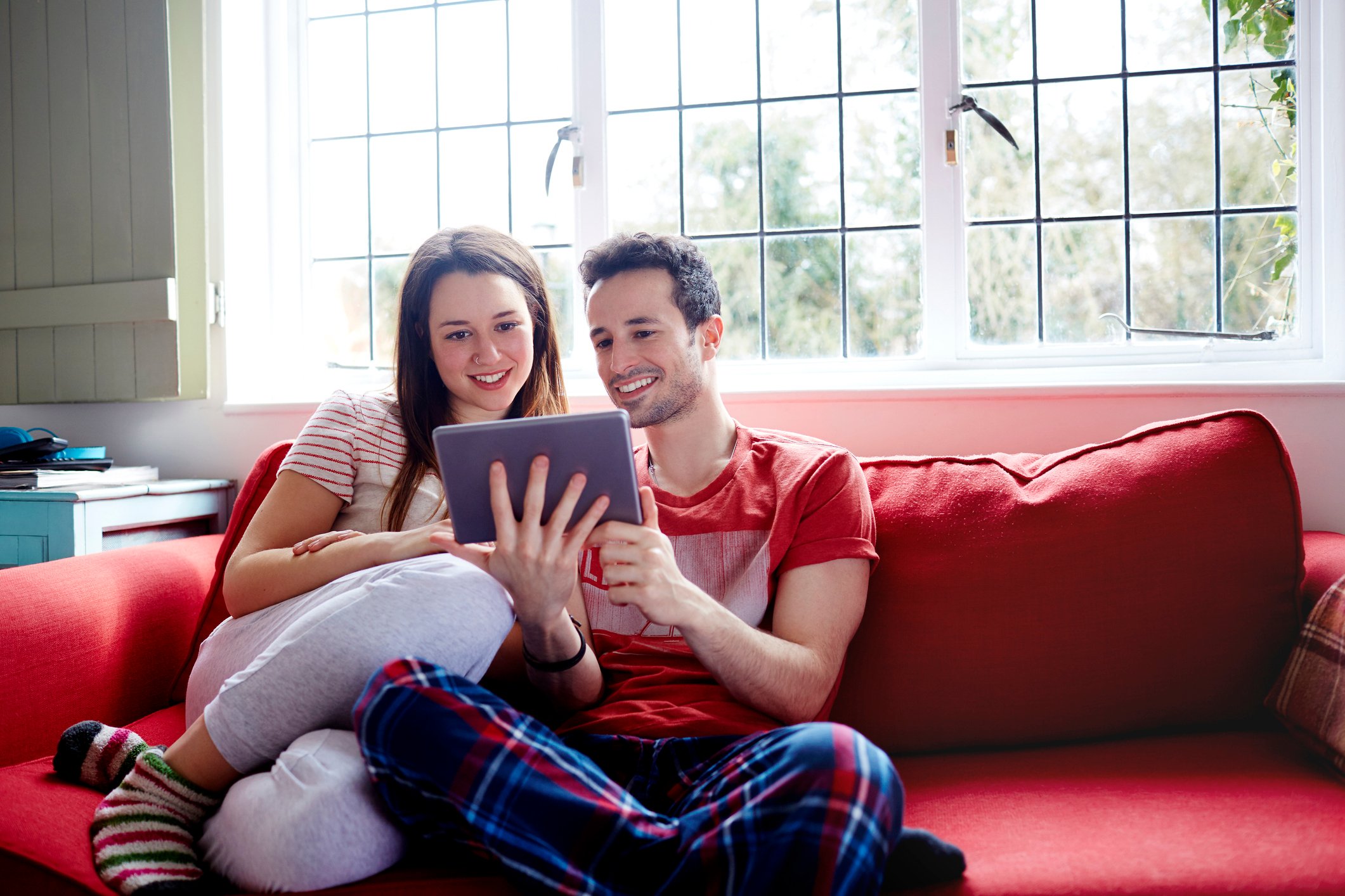 A young couple sitting on a sofa and looking at a tablet computer.