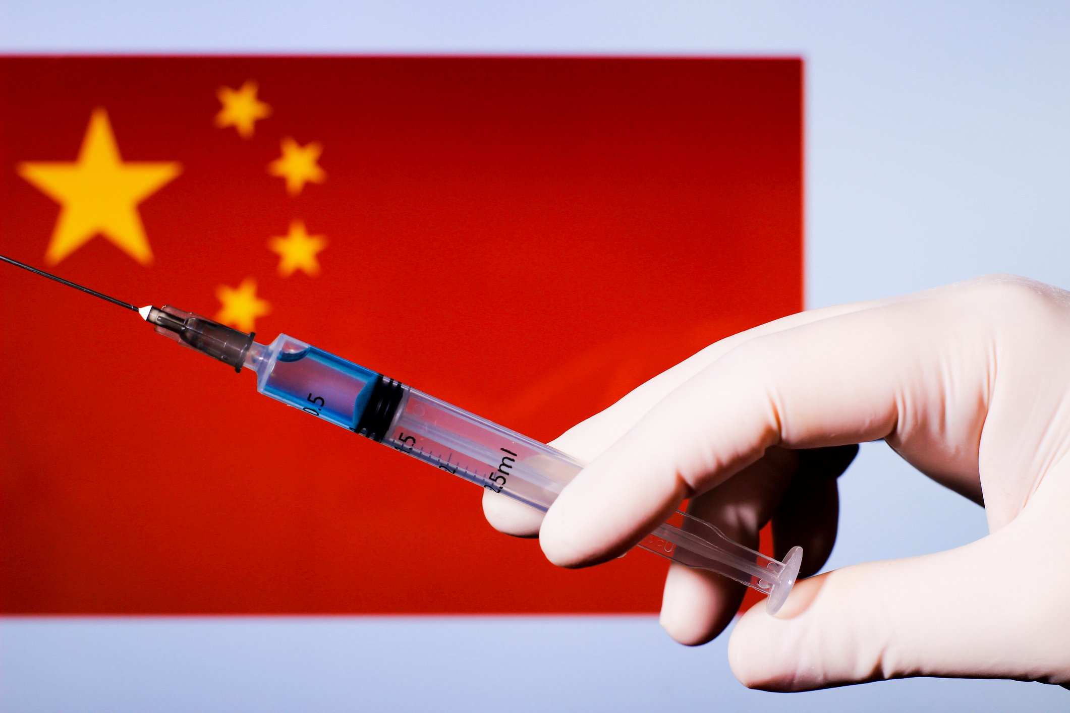Gloved hand holding a syringe with needle with a Chinese flag in the background.