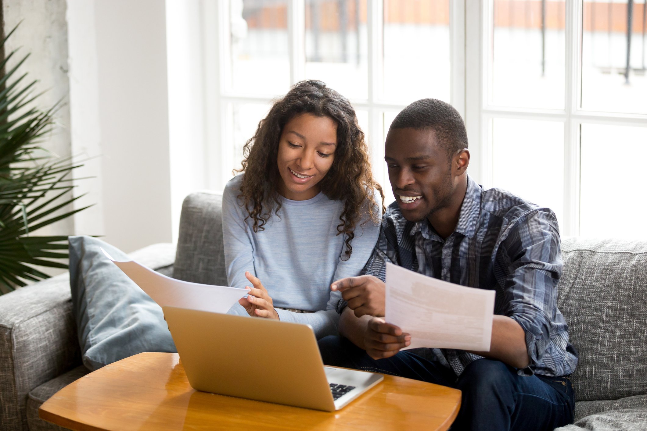 Two smiling people sitting on a sofa while looking at a laptop.