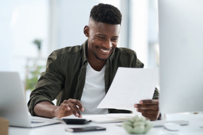 Smiling person looking at financial paperwork and calculator.