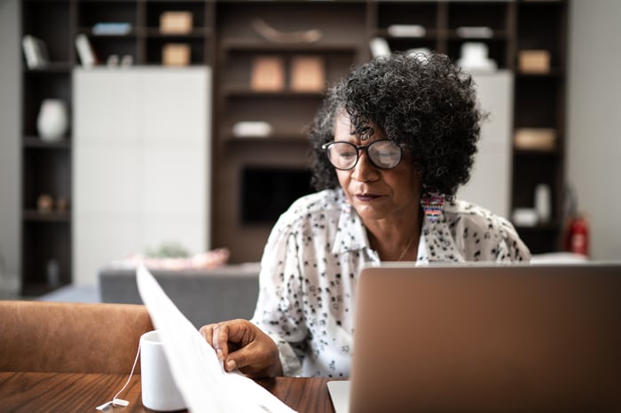 Person looking at financial documents with an open laptop in front of them.