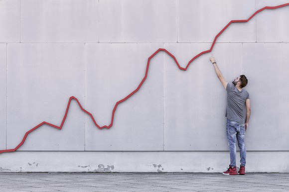 Man pointing toward a rising red line on a wall.