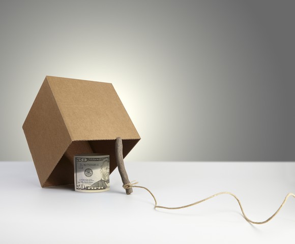 A 50 dollar bill under a cardboard box being propped up with a stick.