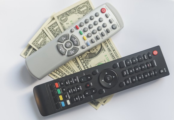 Two TV remotes on a stack of dollar bills.
