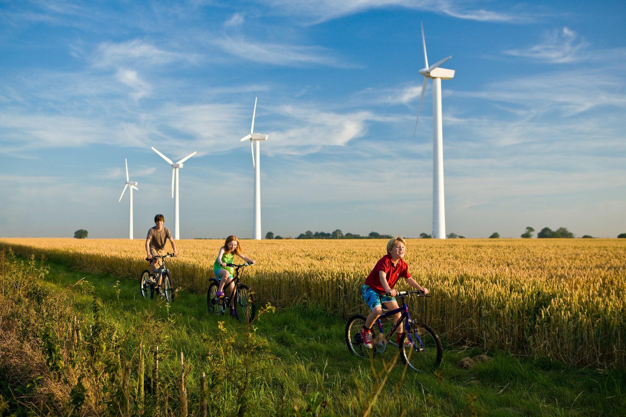 Children cycling past wind turbines.