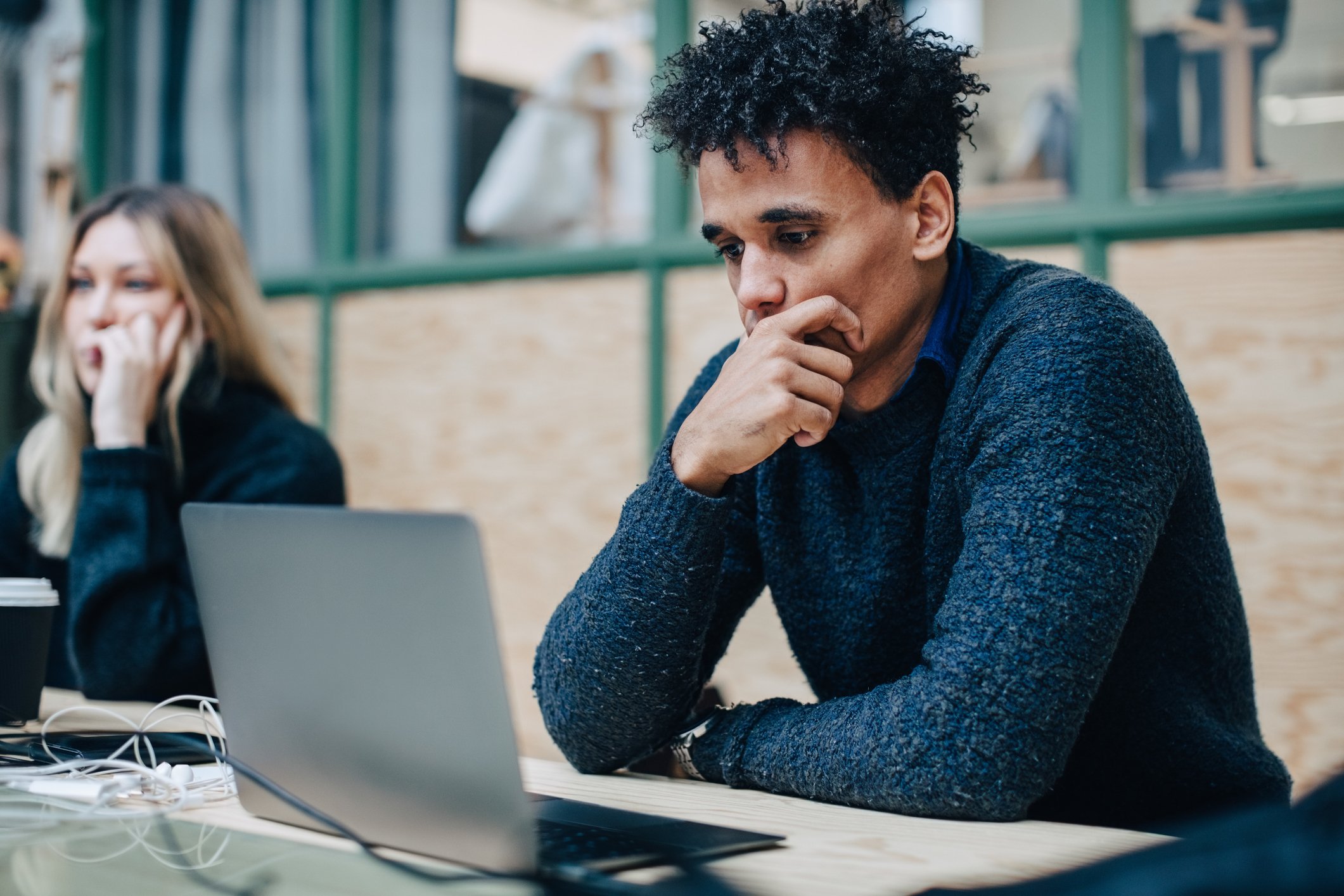 A worried person sitting in front of a laptop, with another person on a phone.