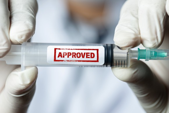 A researcher holds up a vaccine marked "approved."