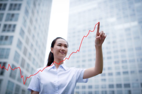 An investor standing against a city background smiles as she traces a line higher in the air.