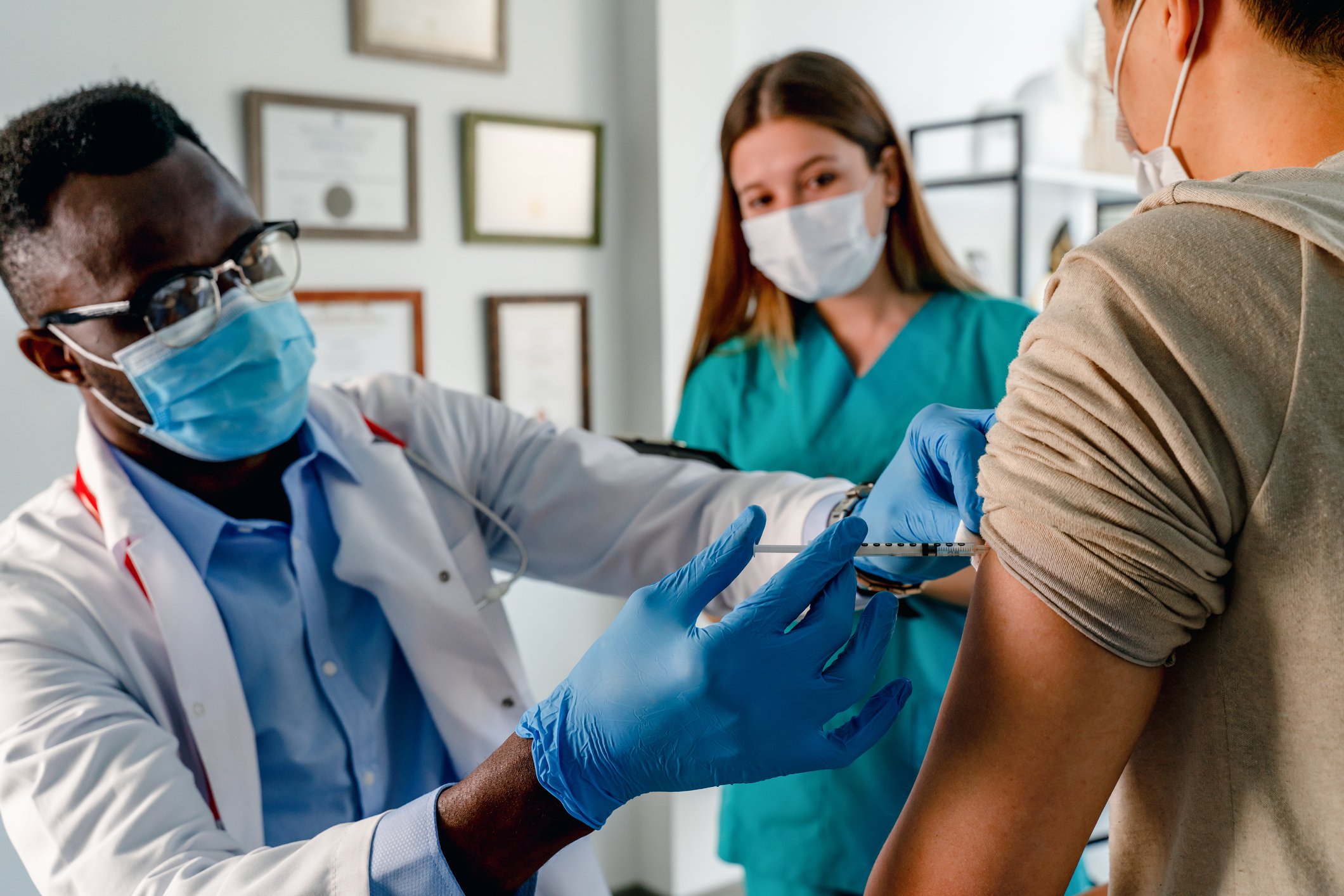 A healthcare professional giving a shot in the arm to a patient with another healthcare professional observing.
