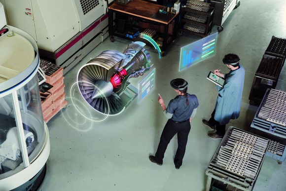 Two people wearing AR headsets view a 3D digital image of an engine in a warehouse.