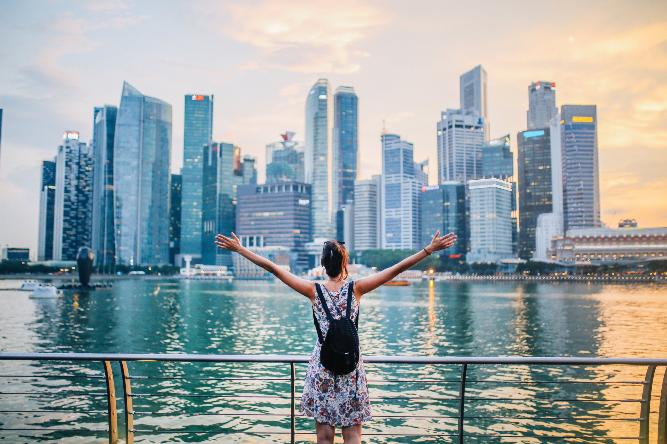 Young person wearing a backpack, arms outstretched, facing the skyline across Singapore Bay.