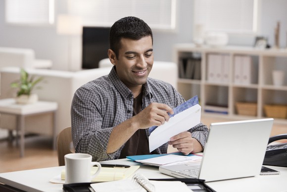 Person opening envelope in front of computer.