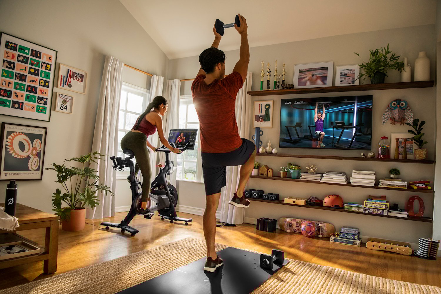 Two people exercise while viewing fitness content from Peloton.