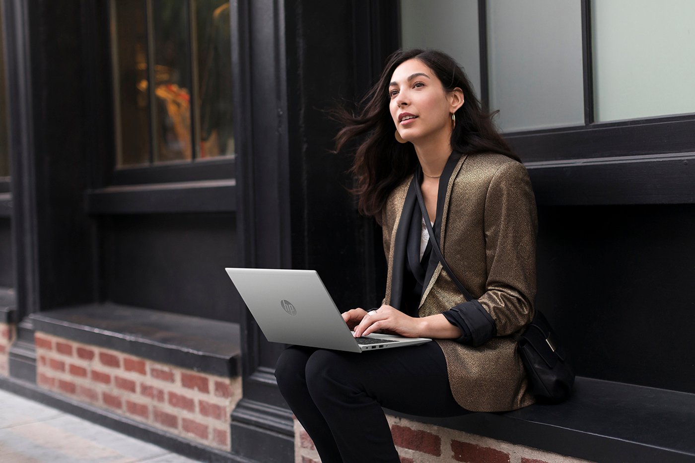 A woman sits on a window ledge looking up to the sky while working on an HP aero G7 laptop