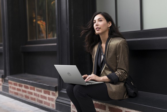 A woman sits on a window ledge looking up to the sky while working on an HP aero G7 laptop