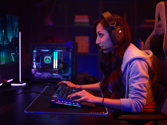 A gamer sits at their keyboard wearing a headset
