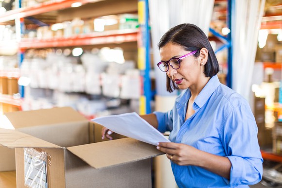 A woman looks at a shipping form in a warehouse. 