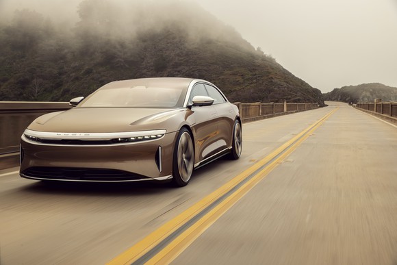 A brown Lucid Air sedan cruises down an open road.