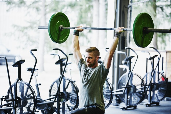 Someone doing barbell lunges at a gym with exercise machines lined up behind them.