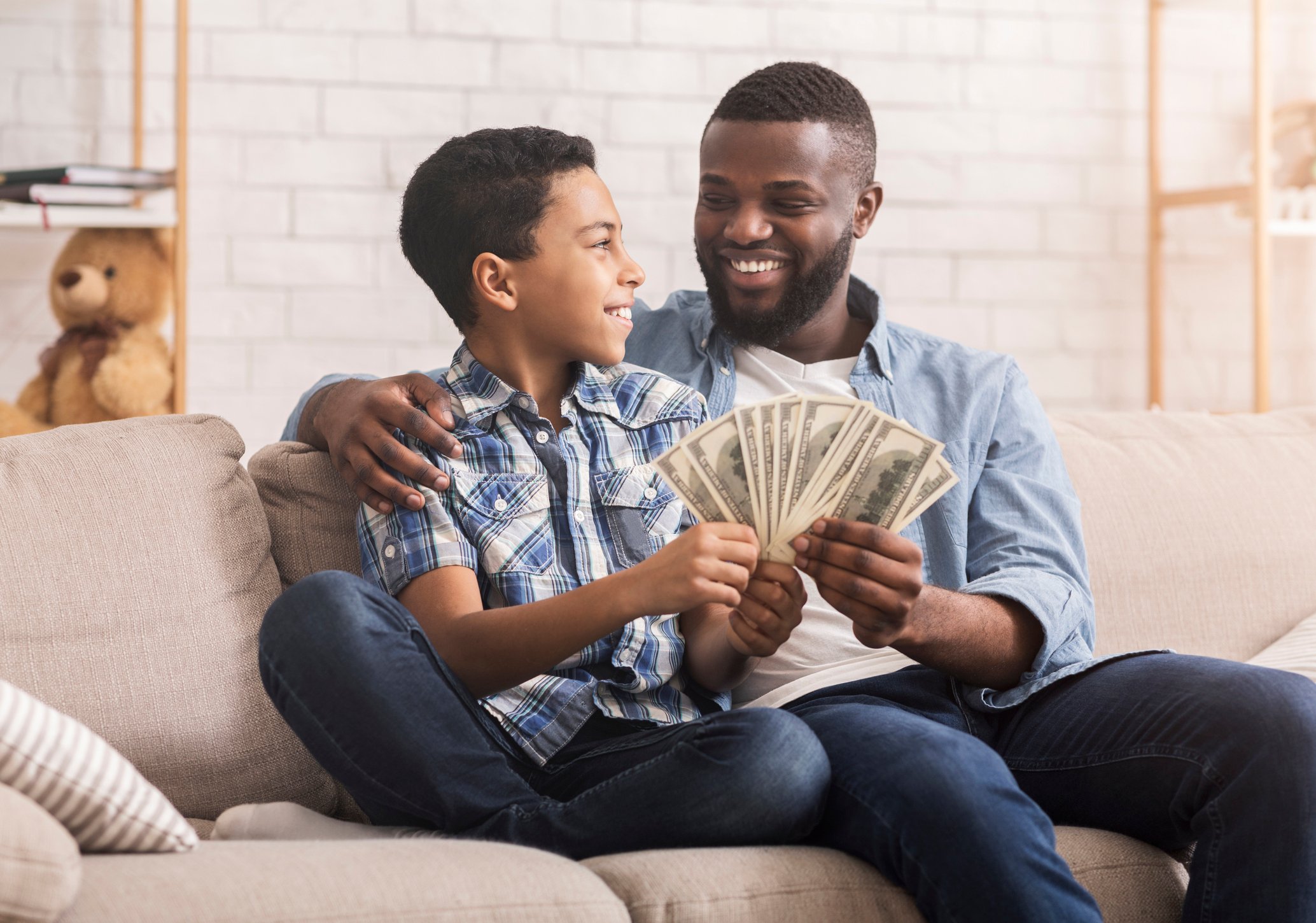A happy adult and child both holding a fan of $100 bills.