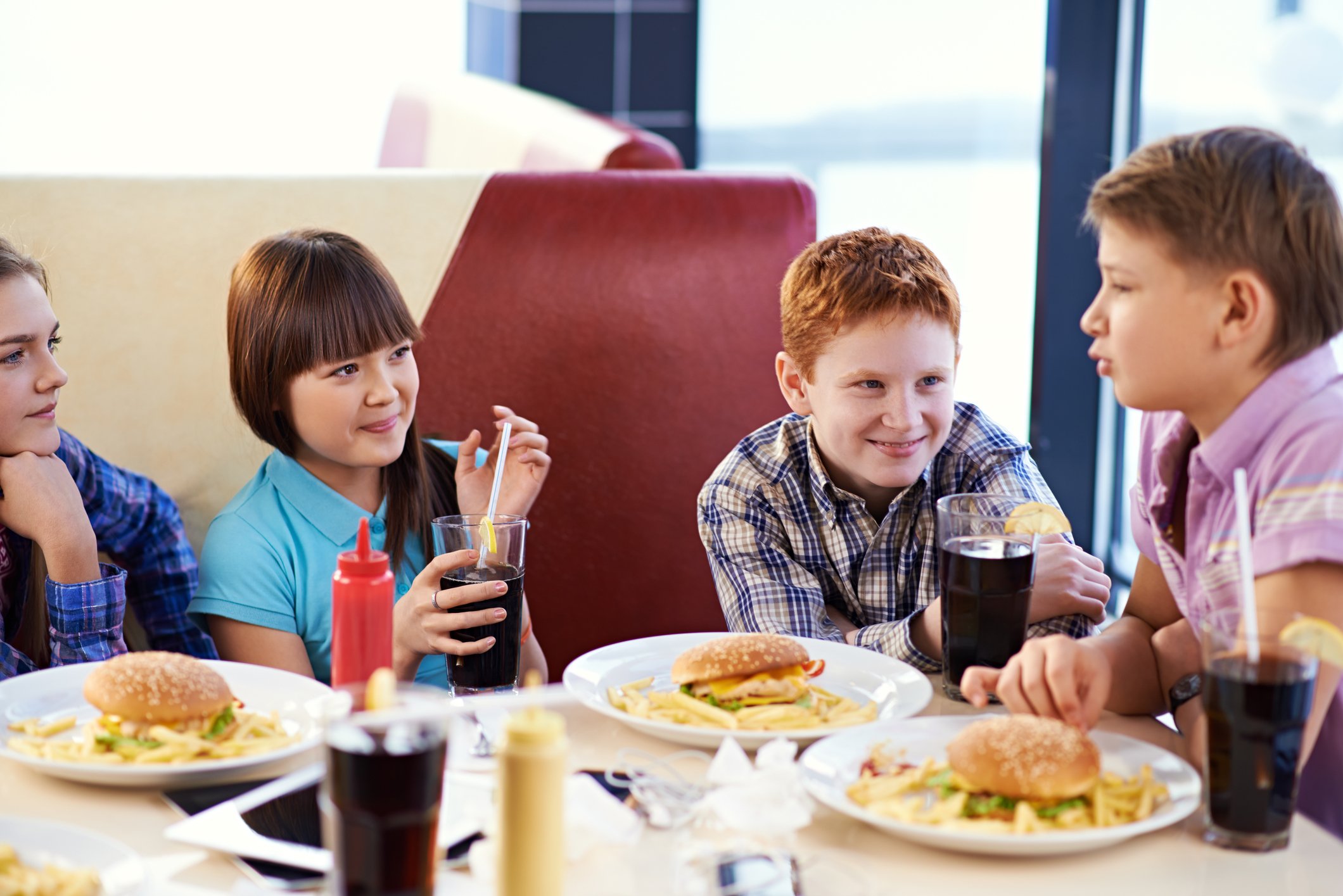 A group of kids eating food and drinking soda at a restaurant.
