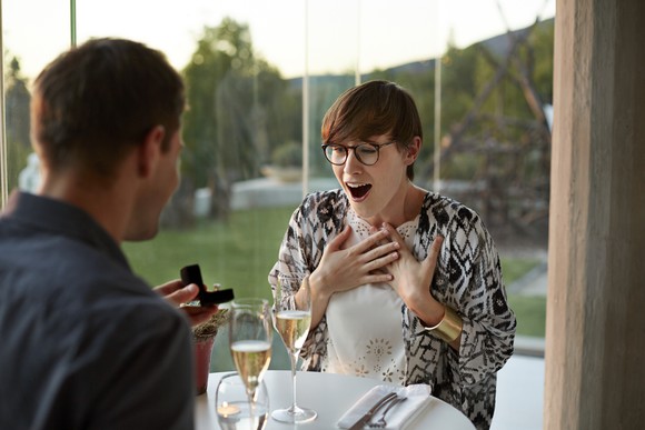 Man giving his surprised girlfriend an engagement ring.