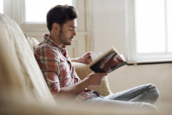 A person sits on a sofa while reading.