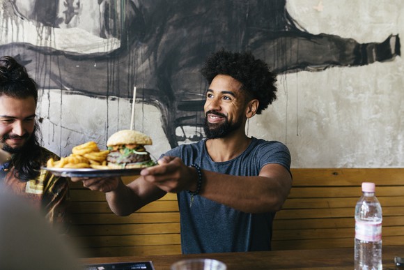 A person being handed a plate with a hamburger and fries in a restaurant.