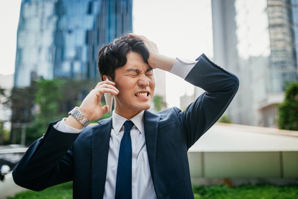 Young businessman in a suit cringes while on cell phone. 