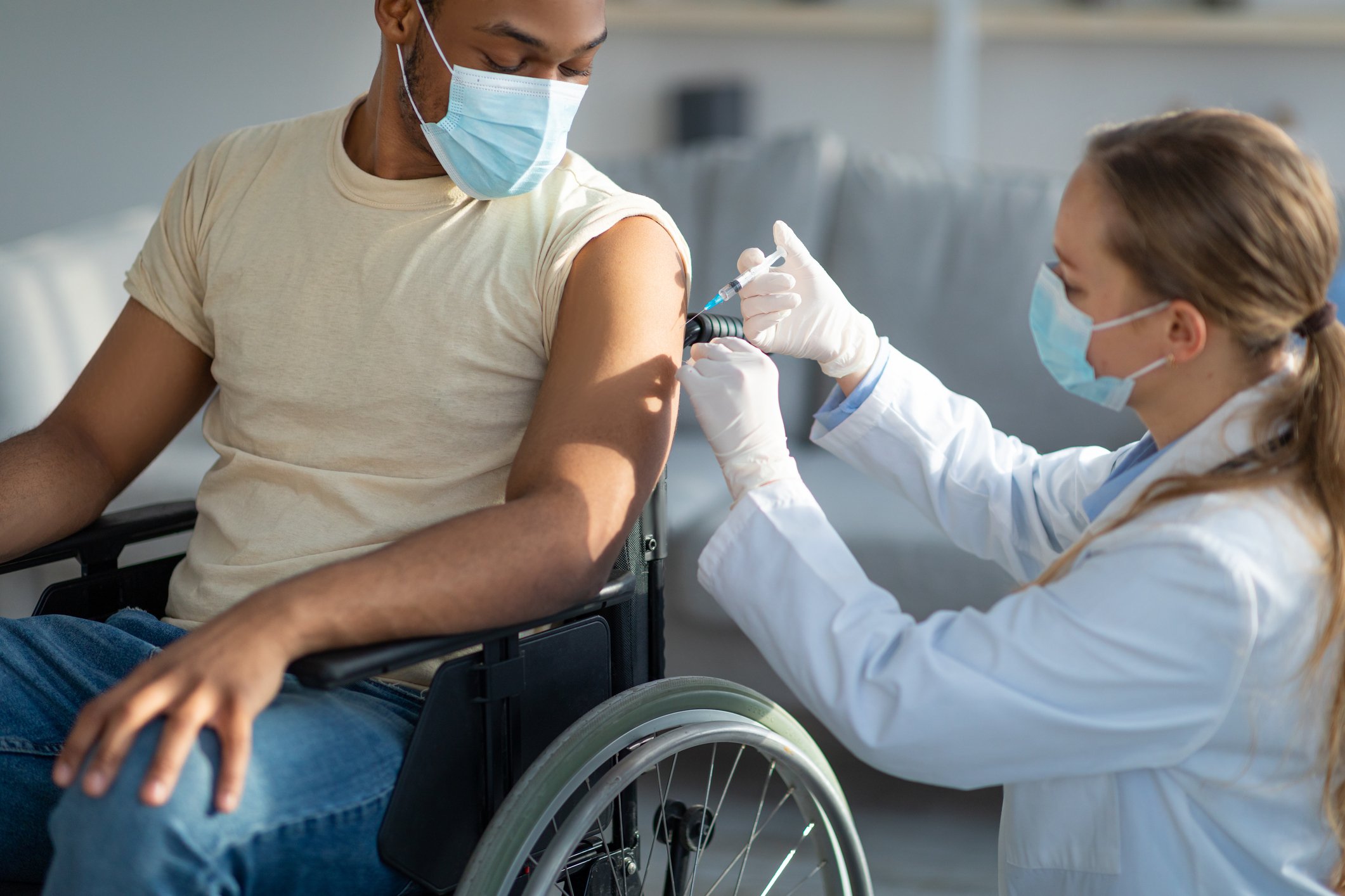 A healthcare worker vaccinates a person seated in a wheelchair.