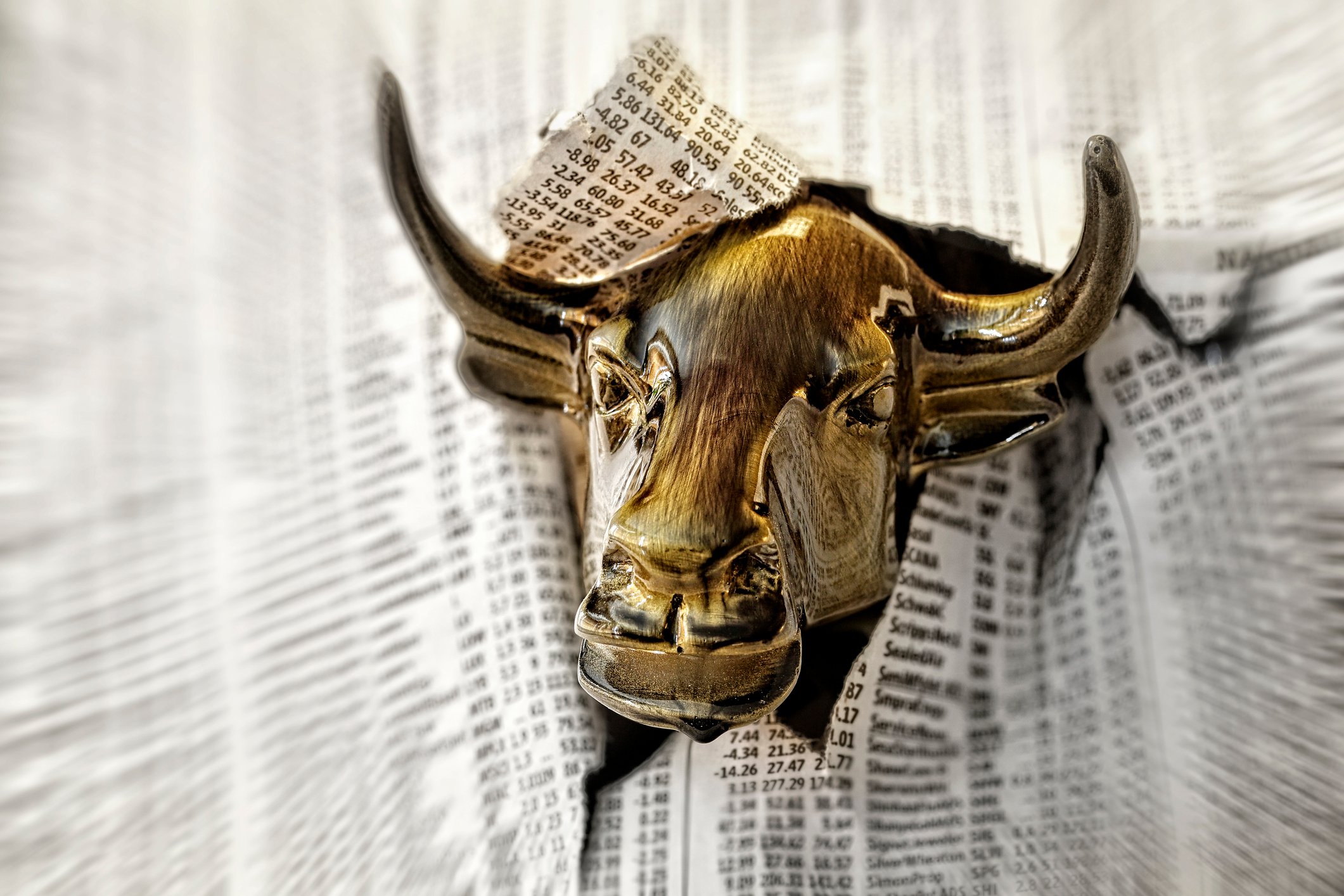 Bull head bursting through stock pages of newspaper