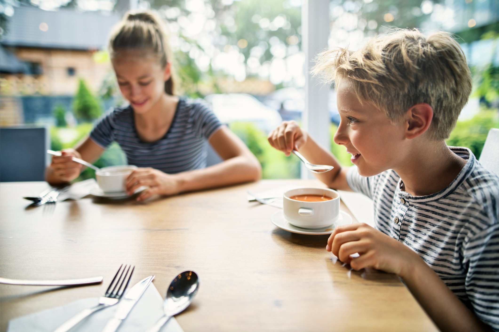 Two children sit at a table eating soup