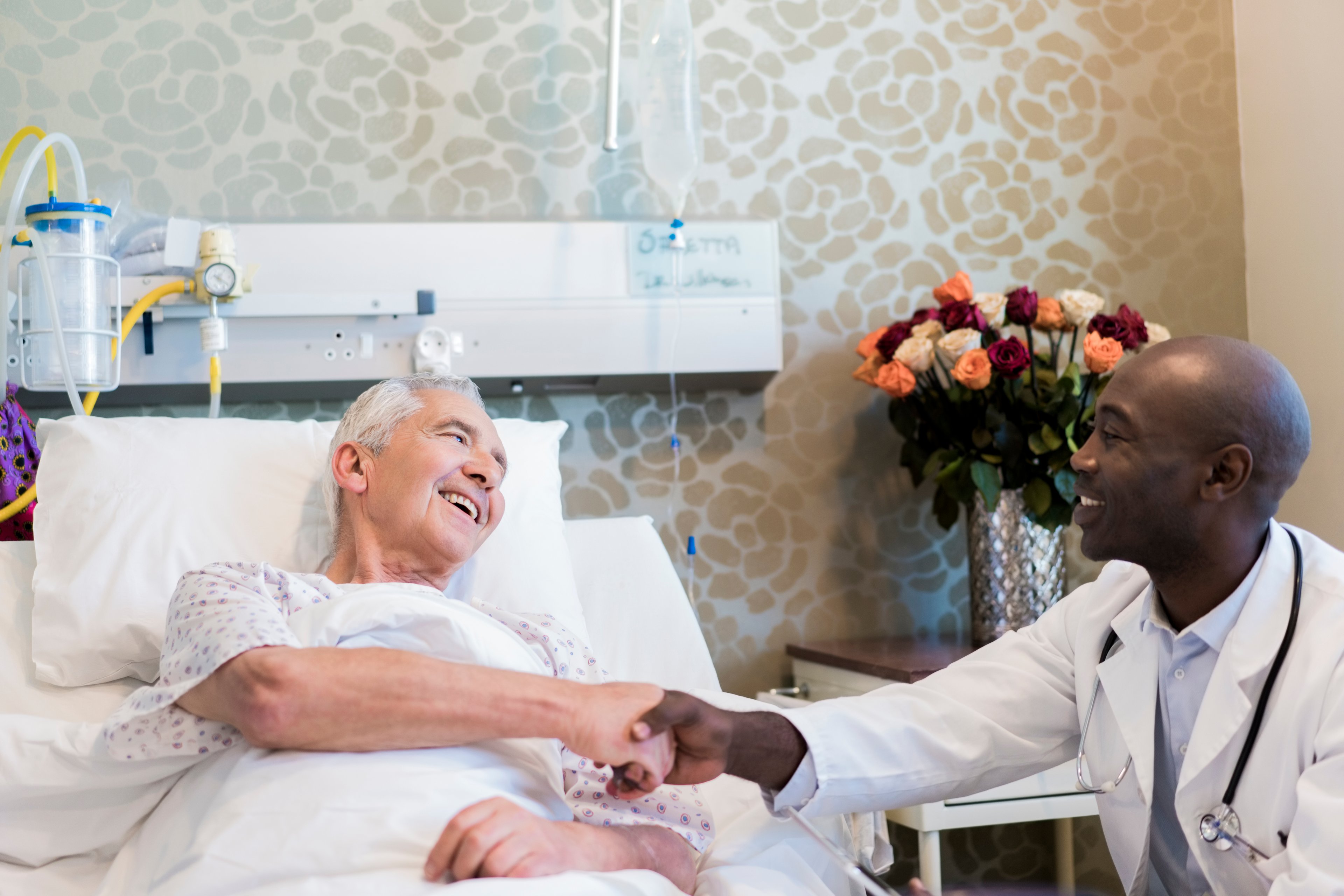 A doctor and a patient in a hospital bed shaking hands. 