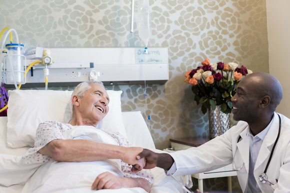 A doctor and a patient in a hospital bed shaking hands. 