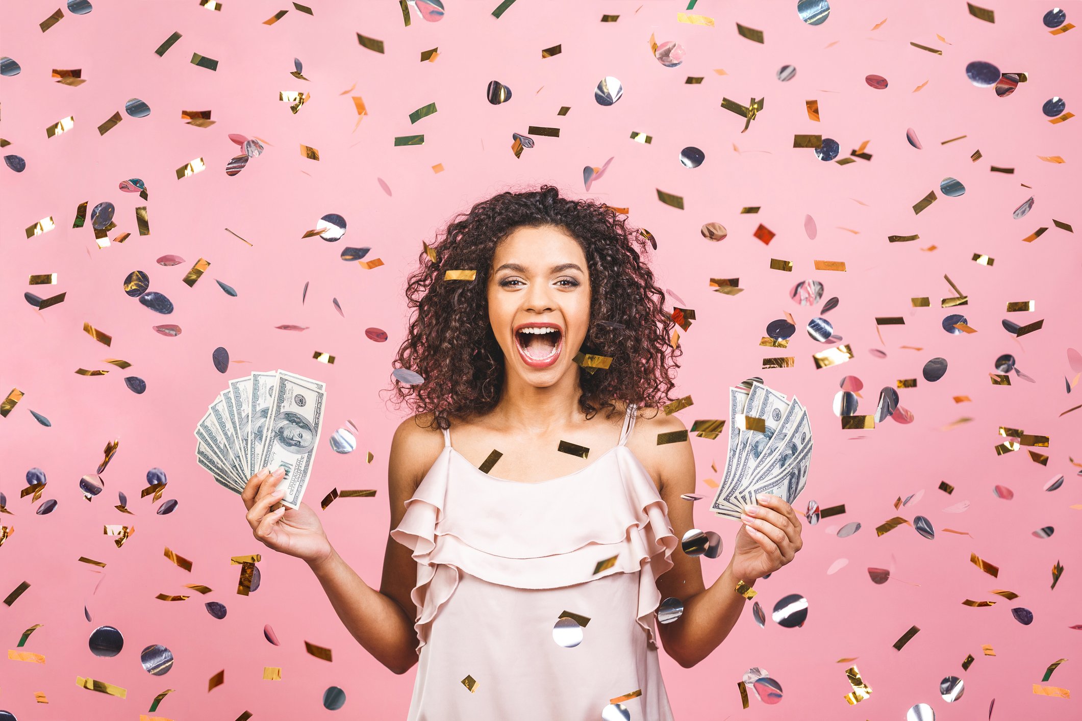 A happy person holding stacks of cash in a shower of confetti.
