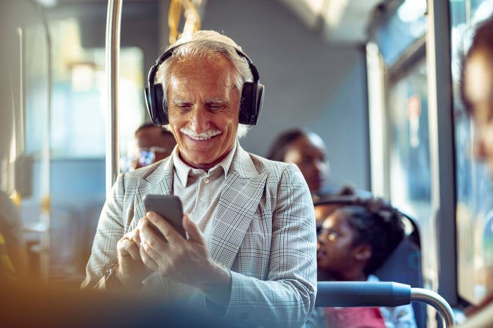 Person wearing headphones looking at smartphone on a bus.