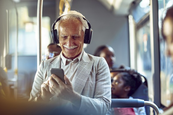 Person wearing headphones looking at smartphone on a bus.