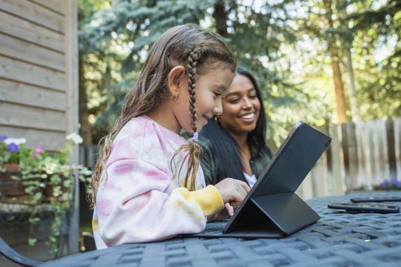 A child sits at a table using a tablet device.