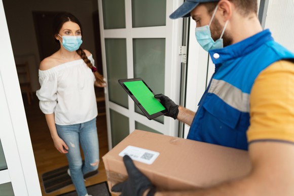 A masked customer opens her door to a masked deliveryman with a box.