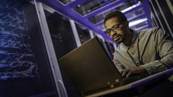 An engineer using a laptop computer in a server room.