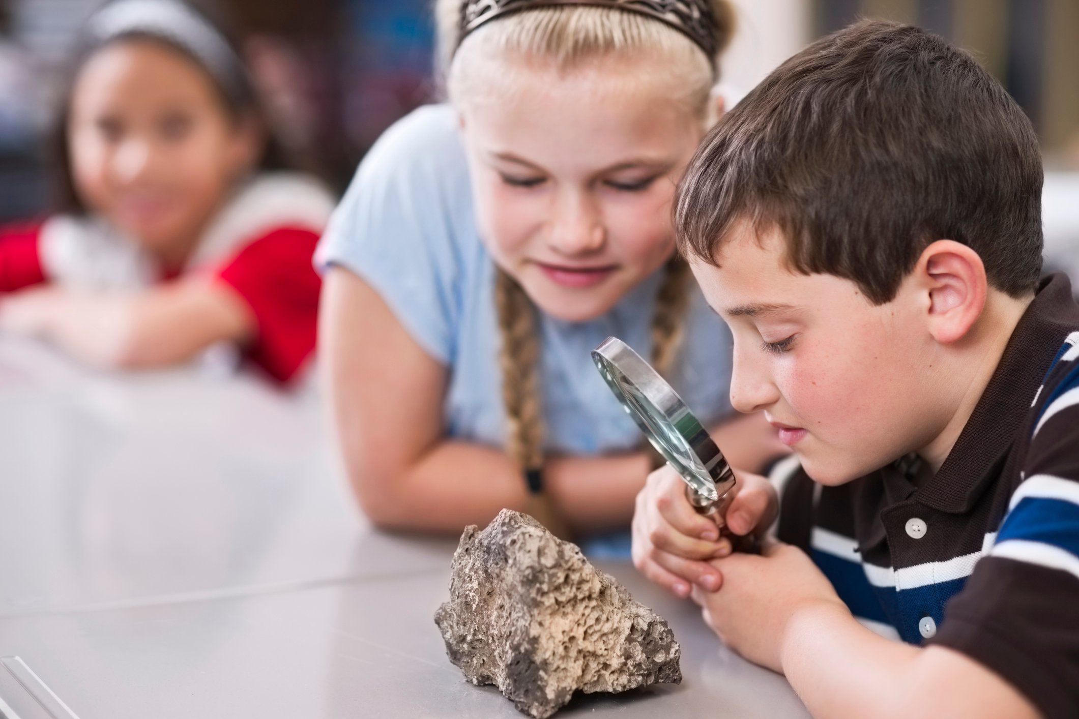 Children using a magnifying glass to get a close look at a small boulder.