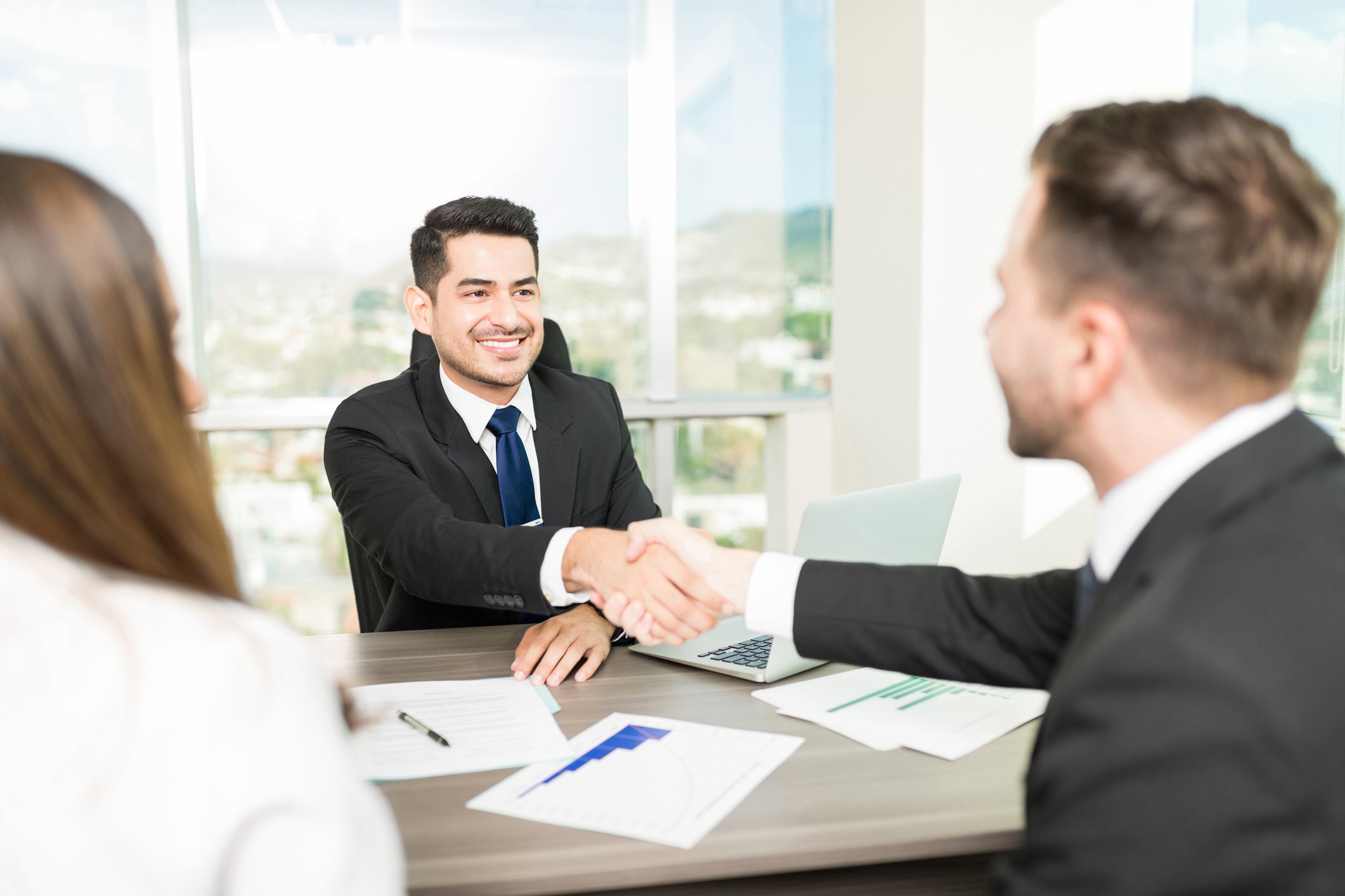 Three people seated around a desk with two of them shaking hands.
