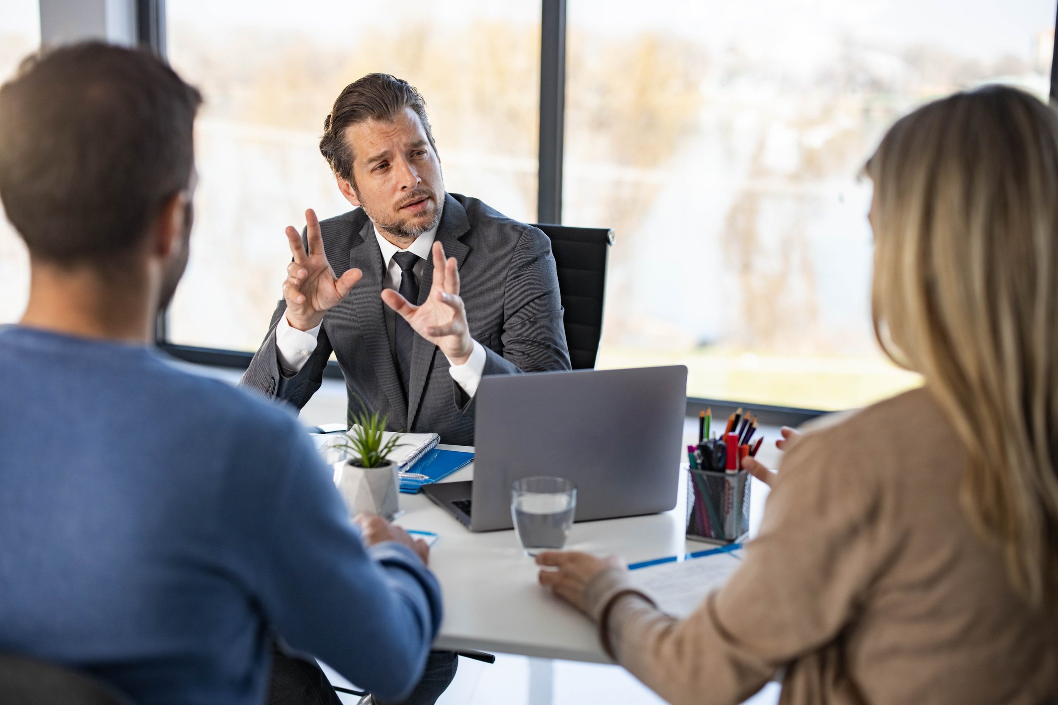 A man in an office talks to two others while they sit at a table.