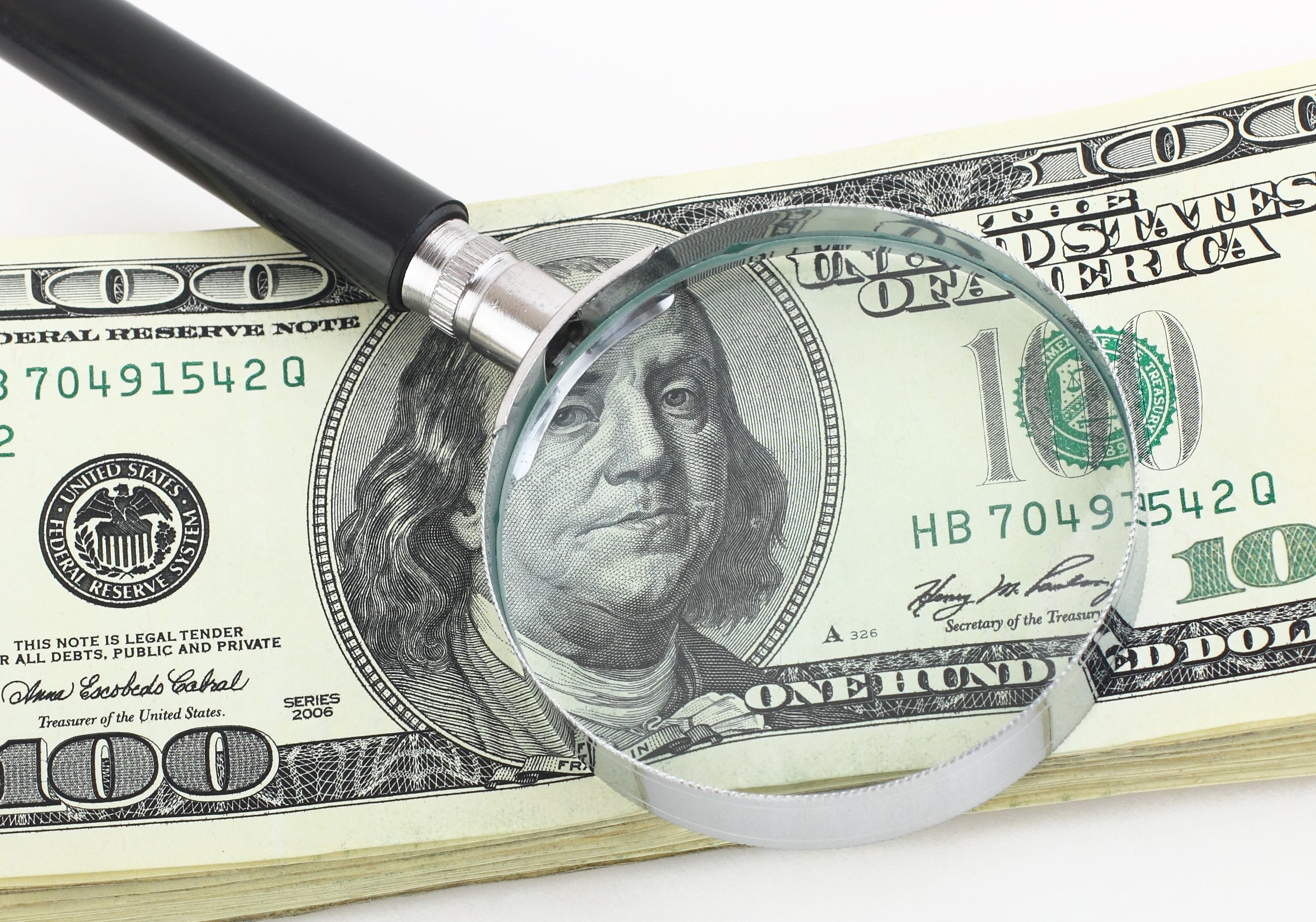A magnifying glass on hundred-dollar bills.