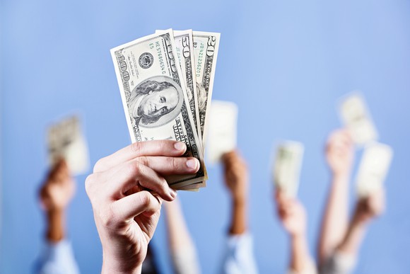 Several hands raised with cash in them.