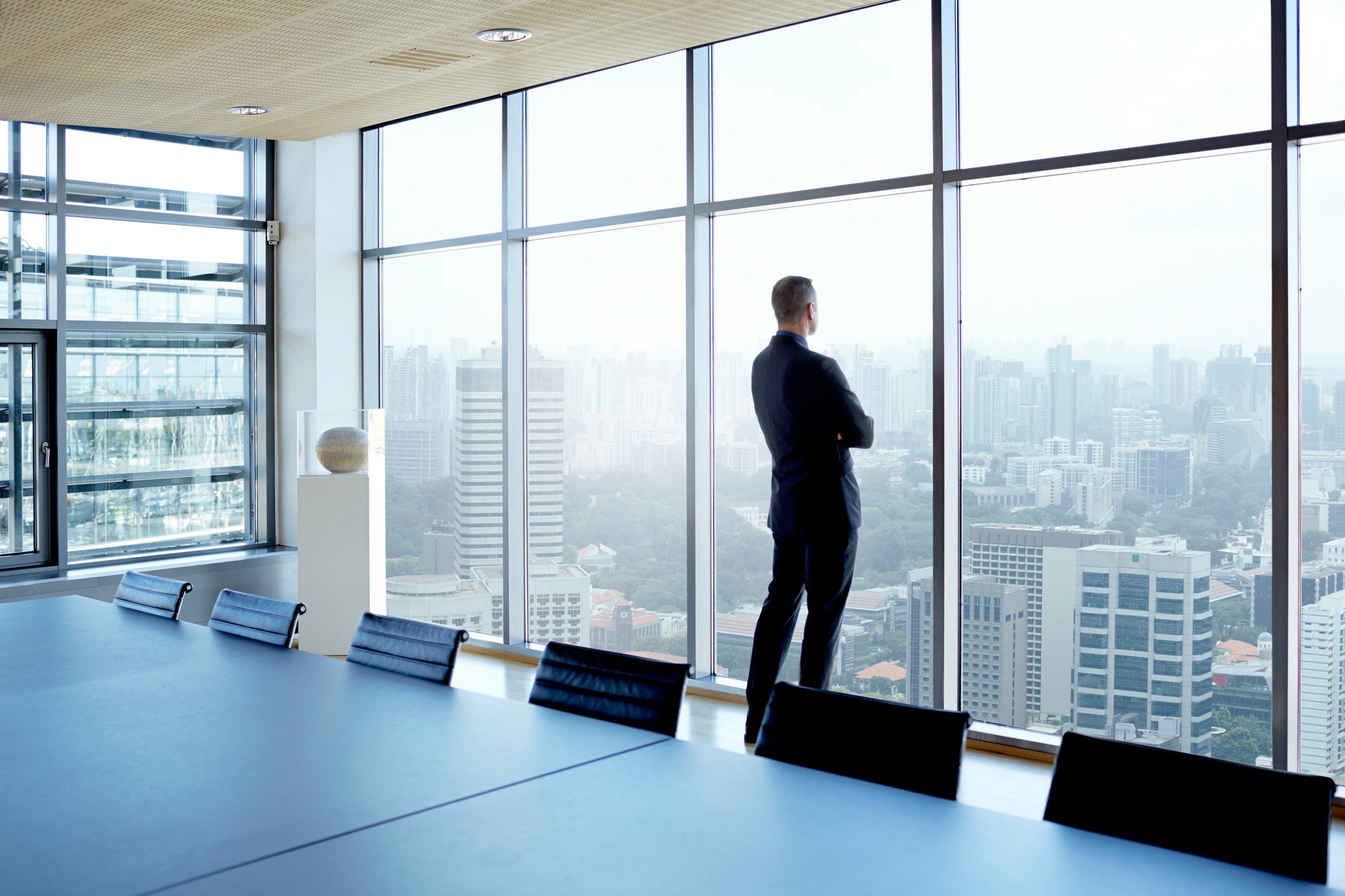 A lone businessperson in an empty boardroom, gazing out thoughtfully from a large window over a city skyline.