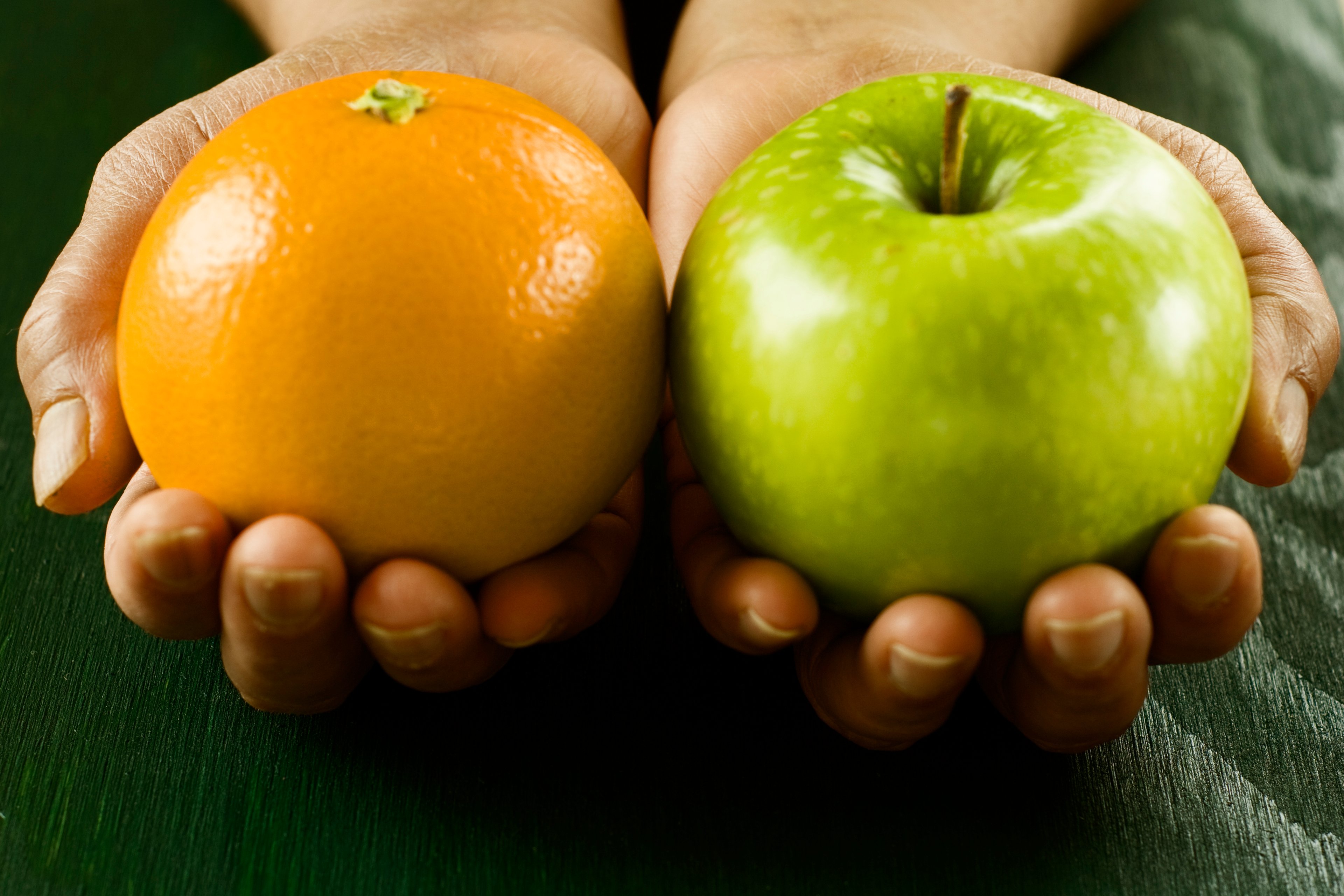 Hands holding an orange and an apple.