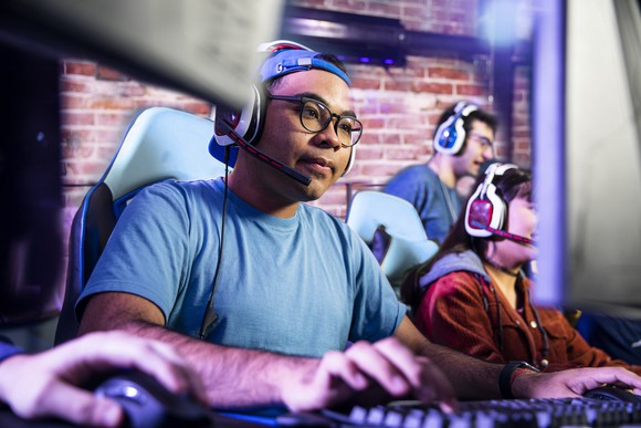 A gamer wearing headphones plays a game on a PC.