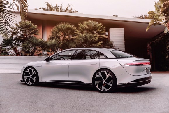 Side view of a white Lucid Air sedan parked in front of a modern home.